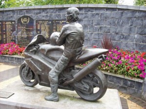 The bronze statue of legendary motorcyclist Joey Dunlop, adorned with flowers, in the tranquil Joey Dunlop Memorial Garden in Ballymoney, Northern Ireland.